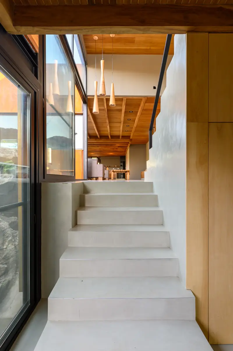 Wood-lined stairway washed in natural light, Casa en Piedras