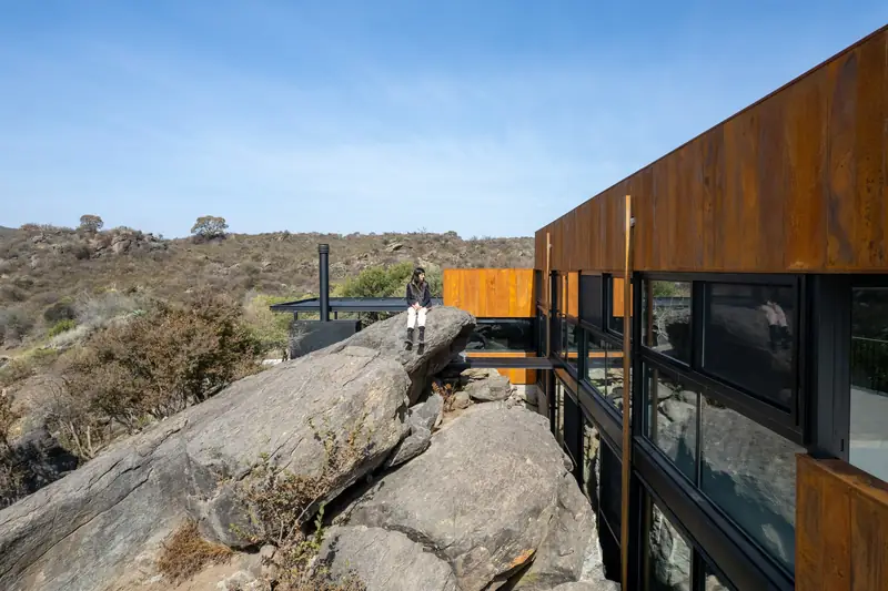 Wood-clad volume cantilevered over boulders, Casa en Piedras